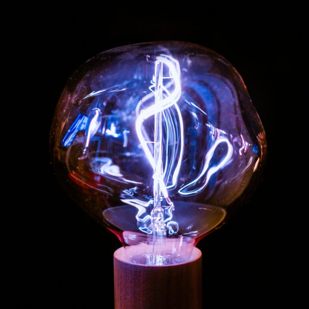 Close-up of a glowing vintage light bulb with an intricate filament design against a dark background.